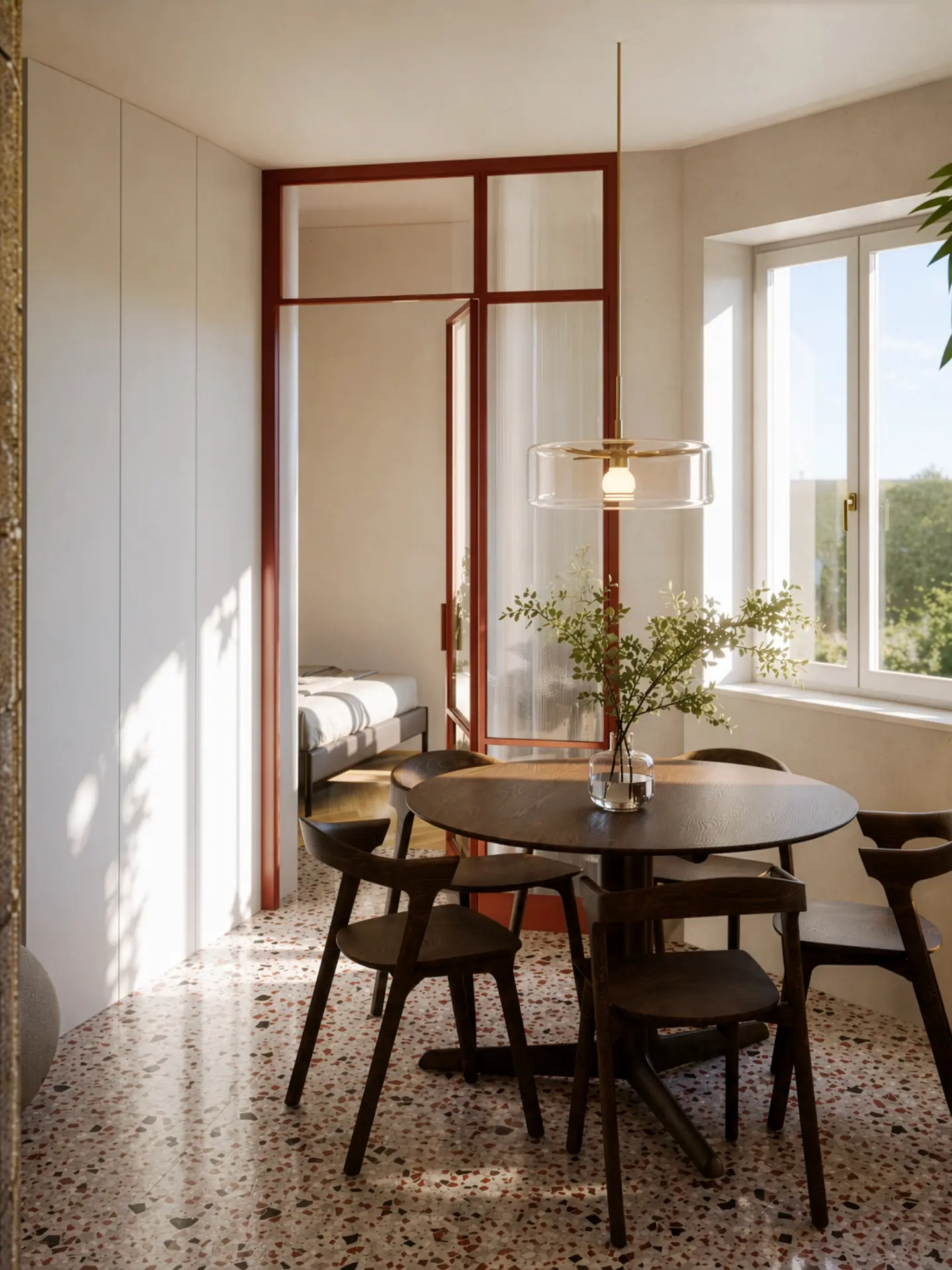 Dining room in a renovated Břevnov apartment with a round dark wood table, terrazzo floor and a rust-red framed glass partition